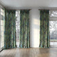 Three patterned curtains hanging in a room with large windows.
