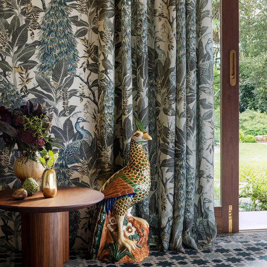 Decorative room with floral-patterned curtains, a wooden table, and a peacock statue.
