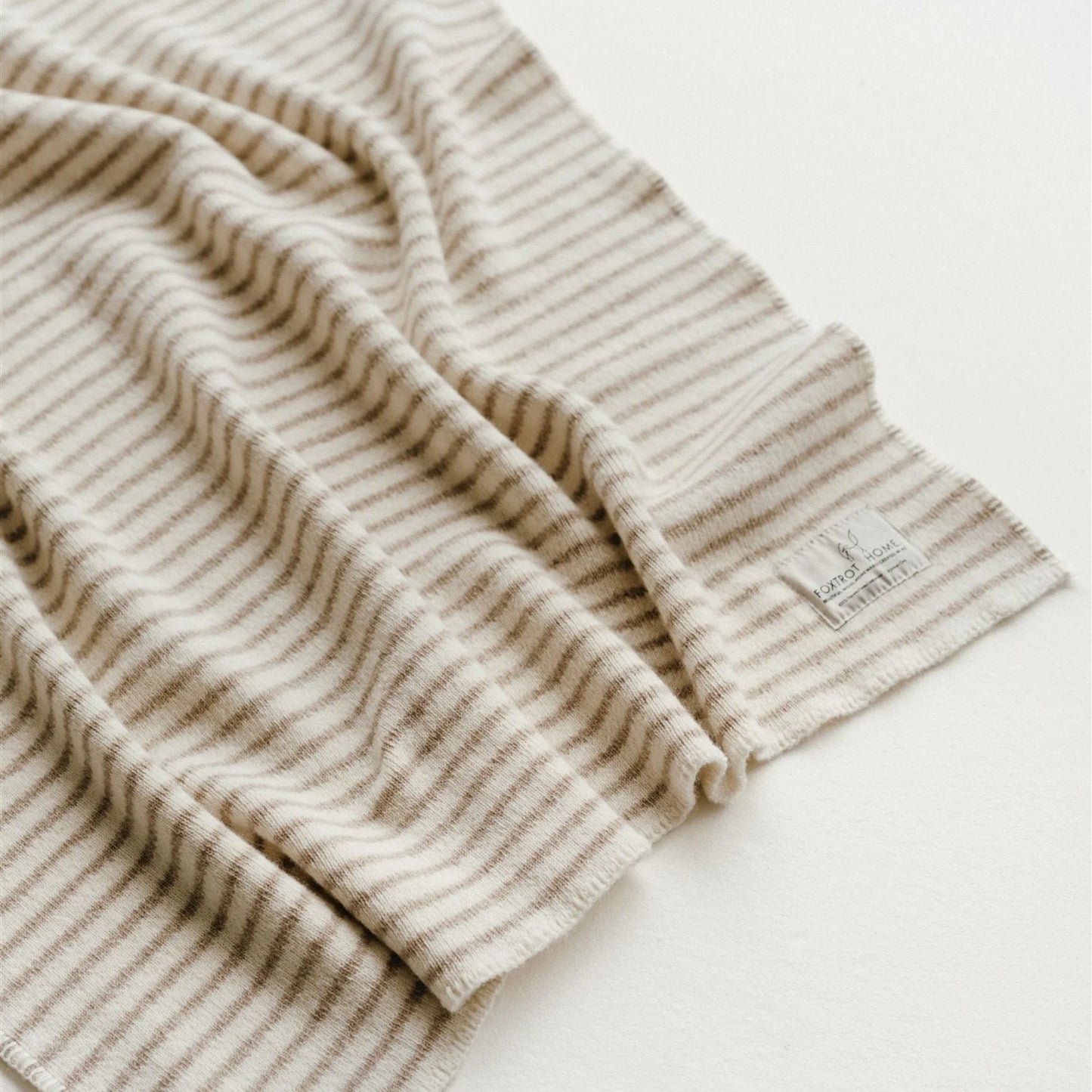 Close-up of a beige and white striped fabric with a brand label on a light background