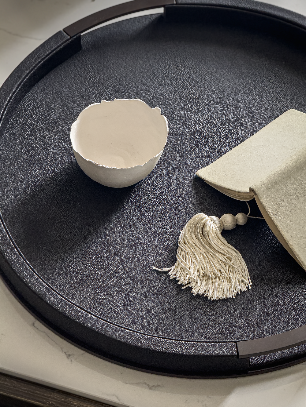 Anthracite shagreen  tray with a white bowl, beige pouch, and tassel on a light background