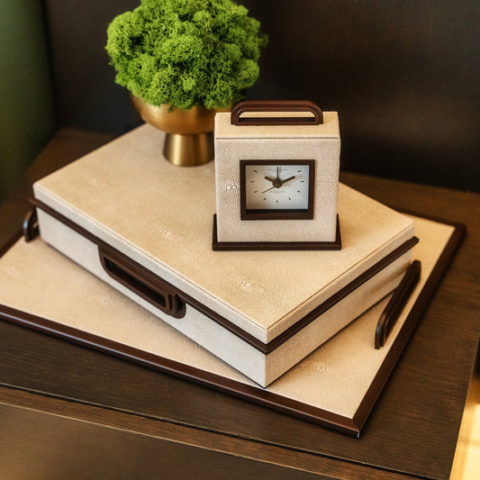 Decorative stack of books with a clock and plant on a wooden surface