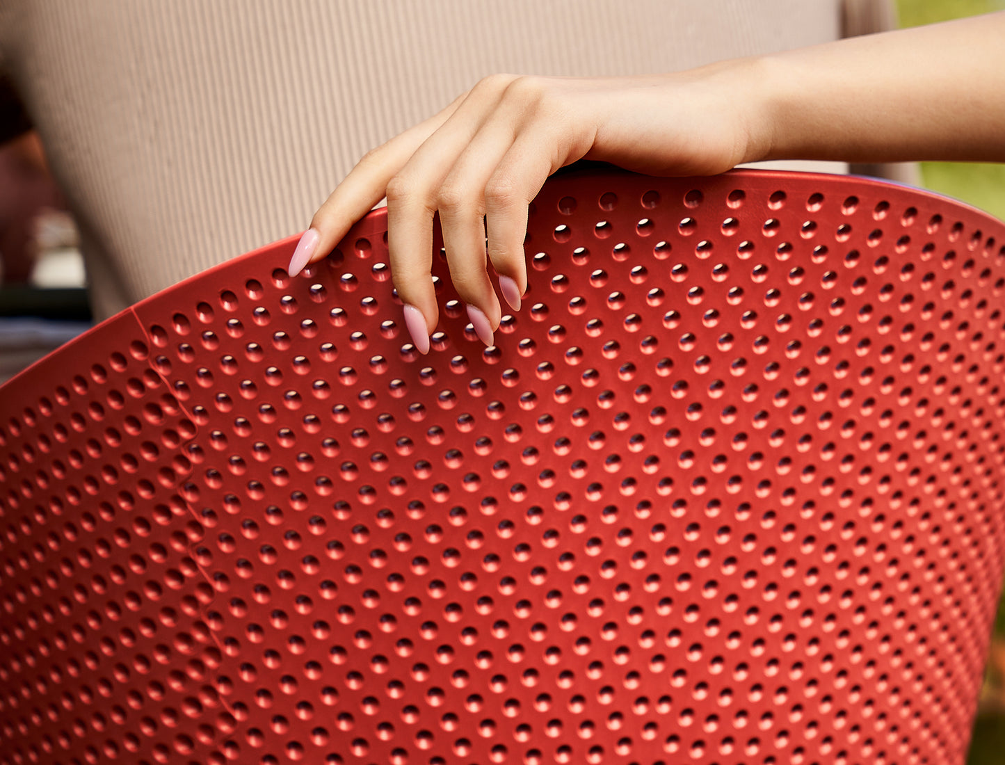 Close-up of a hand holding a red perforated chair