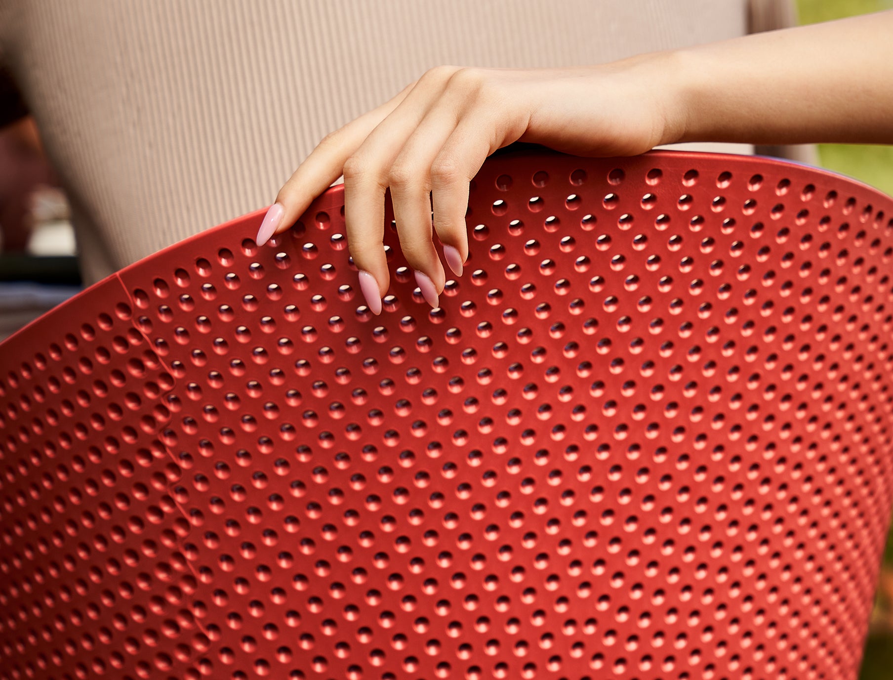Close-up of a hand holding a red perforated chair