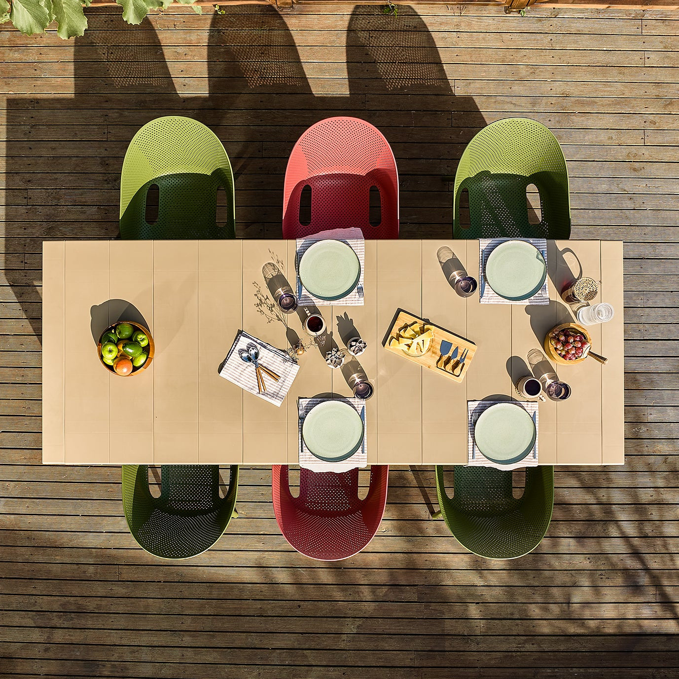 Top-down view of a dining table with plates, cups, and food on a wooden deck.