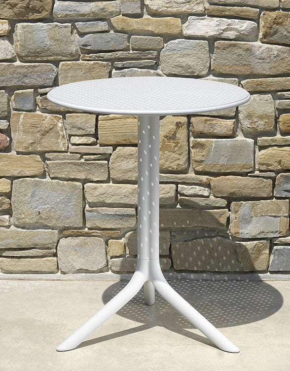 White round table with a star-shaped base against a stone wall.