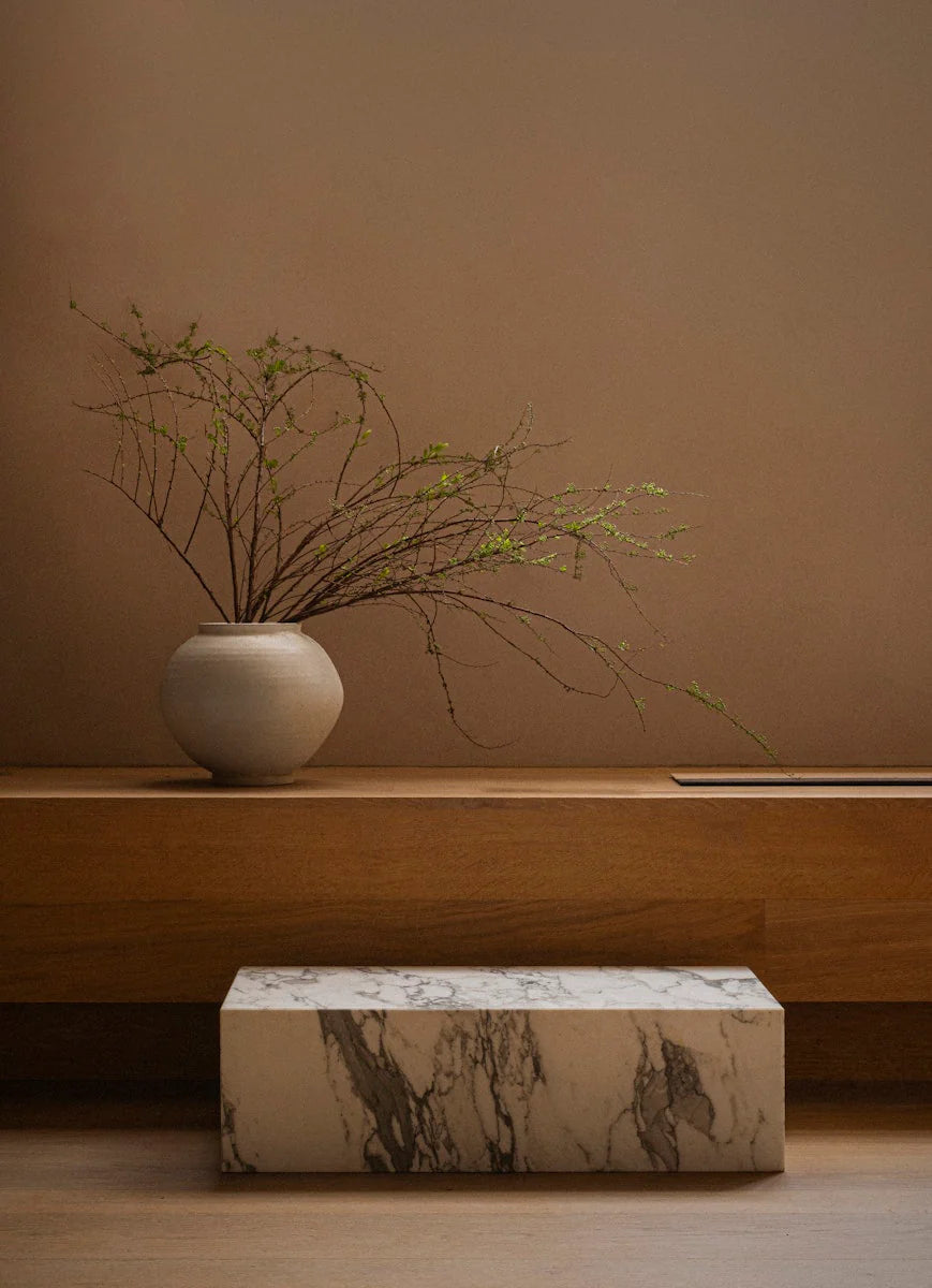 Vase with branches on a wooden shelf against a beige wall