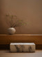 Vase with branches on a wooden shelf against a beige wall