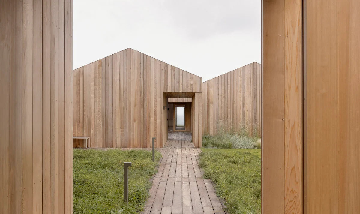 Wooden architectural structure with a pathway leading into it, surrounded by grass.