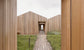 Wooden architectural structure with a pathway leading into it, surrounded by grass.
