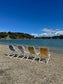 Colorful beach chairs on a pebbly beach with a body of water and trees in the background.
