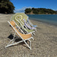 Beach chairs and an umbrella on a pebbly beach with trees and water in the background.