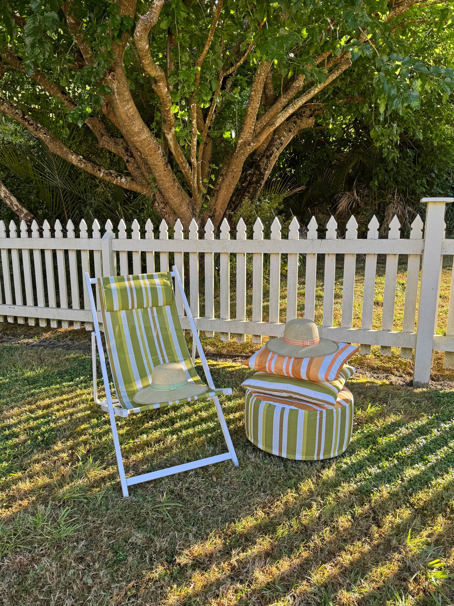 Striped deck chair and ottoman on grass with white picket fence and tree in background