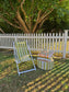 Striped deck chair and ottoman on grass with white picket fence and tree in background