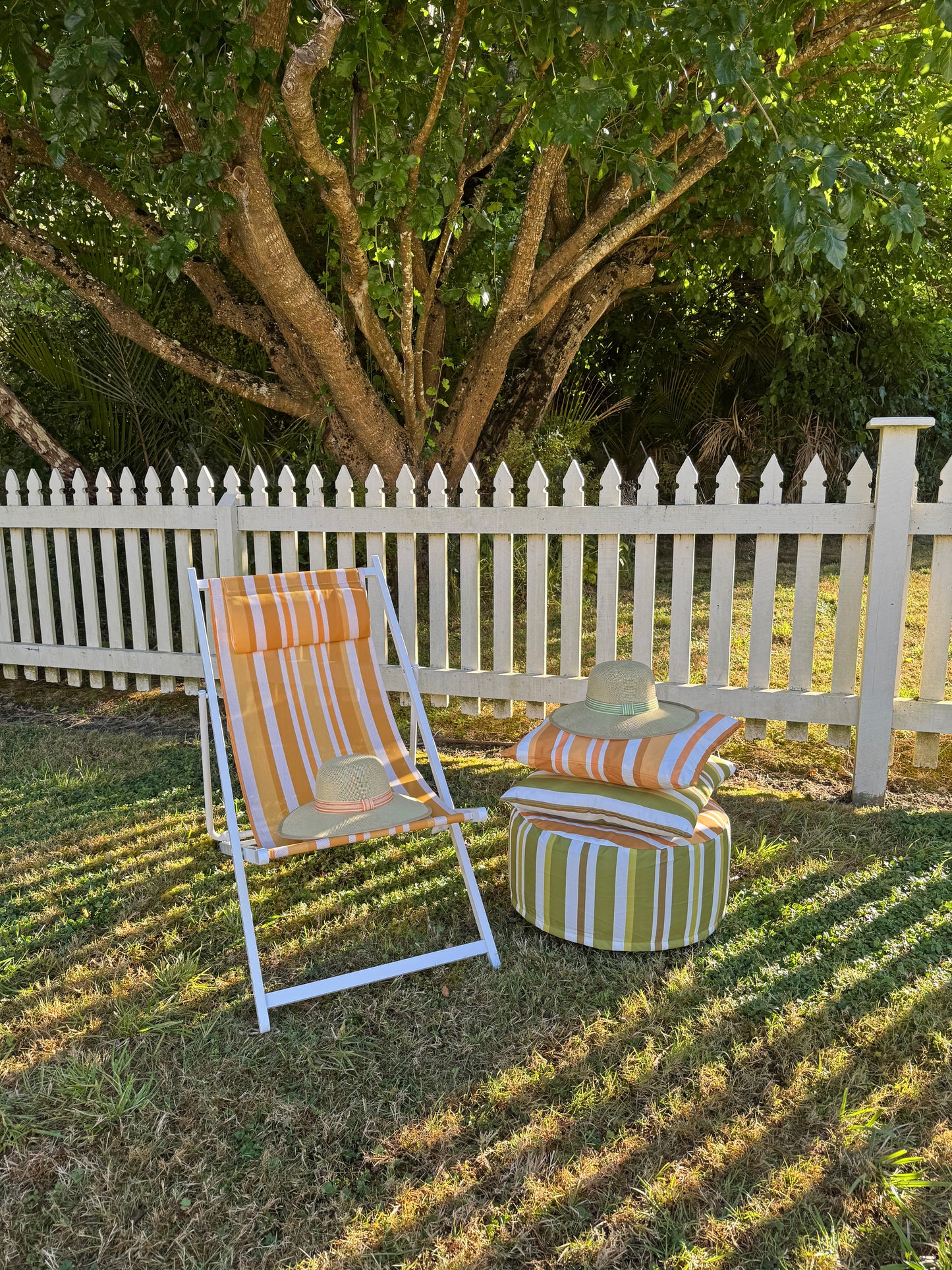 Outdoor furniture set with striped chair and ottoman on grass, white picket fence in background
