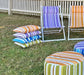 Colorful outdoor chairs and ottomans on grass with a white picket fence and tree in the background