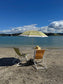 Two beach chairs with a striped umbrella on a sandy beach with a scenic view of water and sky.
