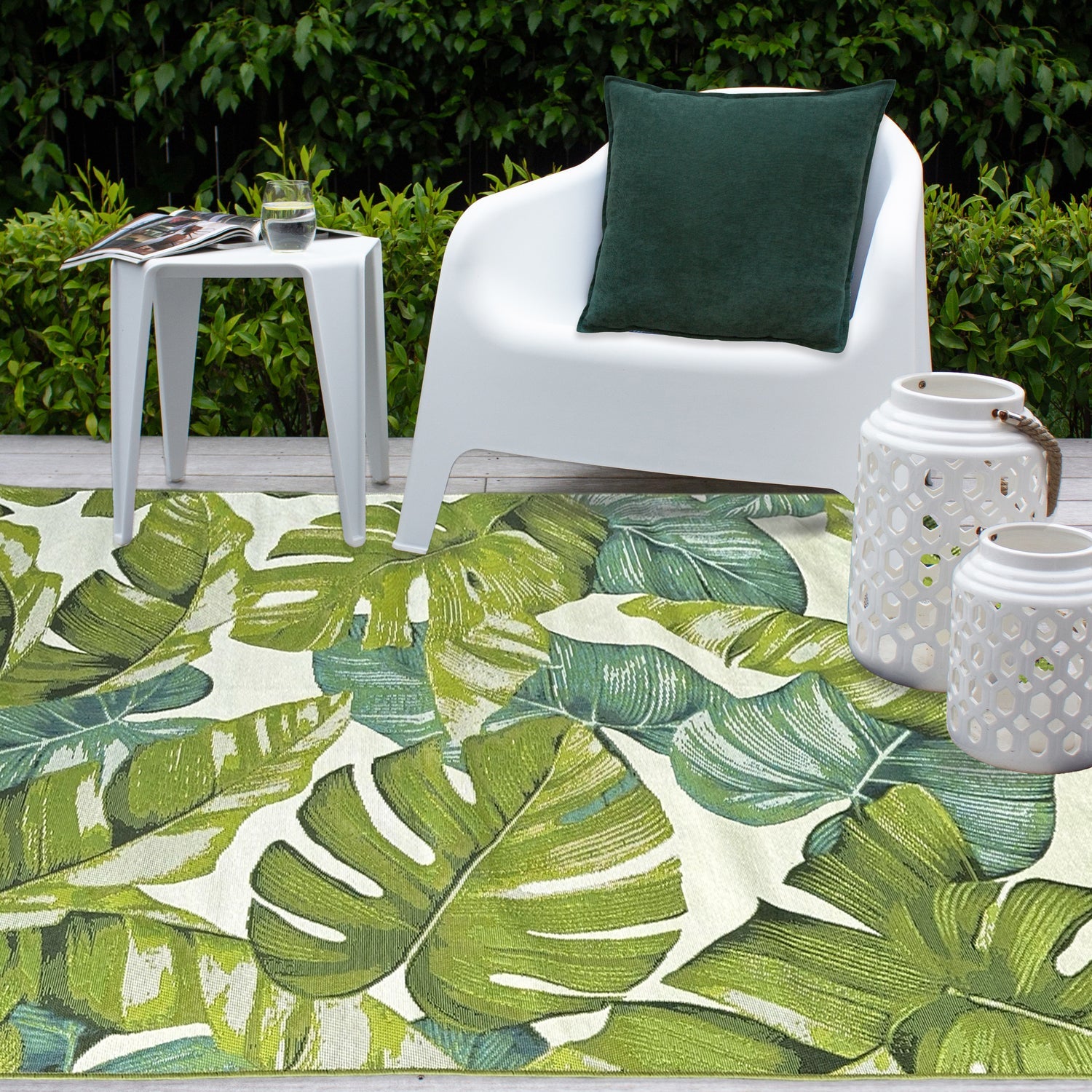 Tropical leaf patterned rug with a white chair and green pillow in a garden setting.