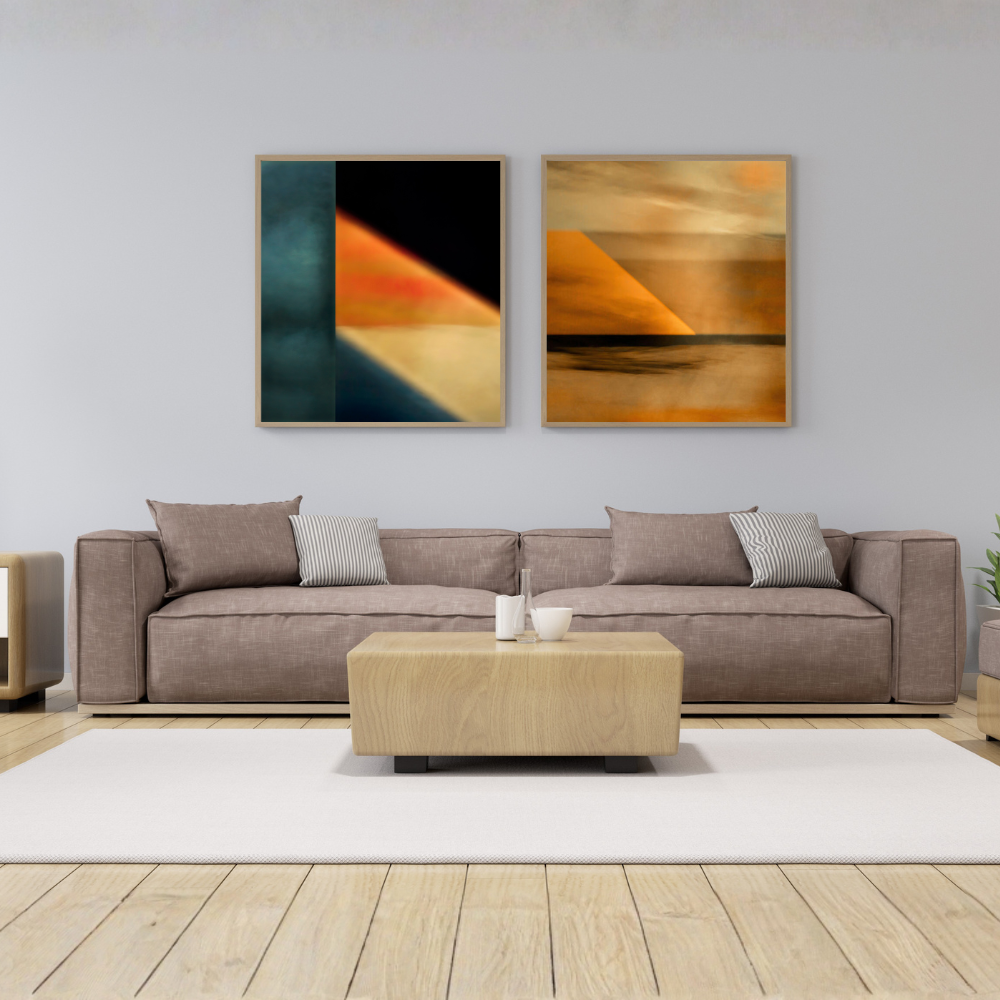 A modern living room setup featuring two framed abstract art prints hanging on a light gray wall above a brown fabric sofa. The left print has geometric blocks of teal, black, orange, and beige, while the right print shows an abstract landscape with orange and beige tones.