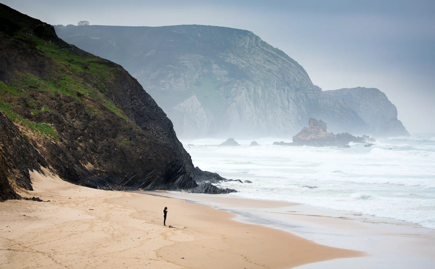 Person standing on a beach with cliffs and ocean waves in the background