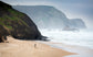 Person standing on a beach with cliffs and ocean waves in the background