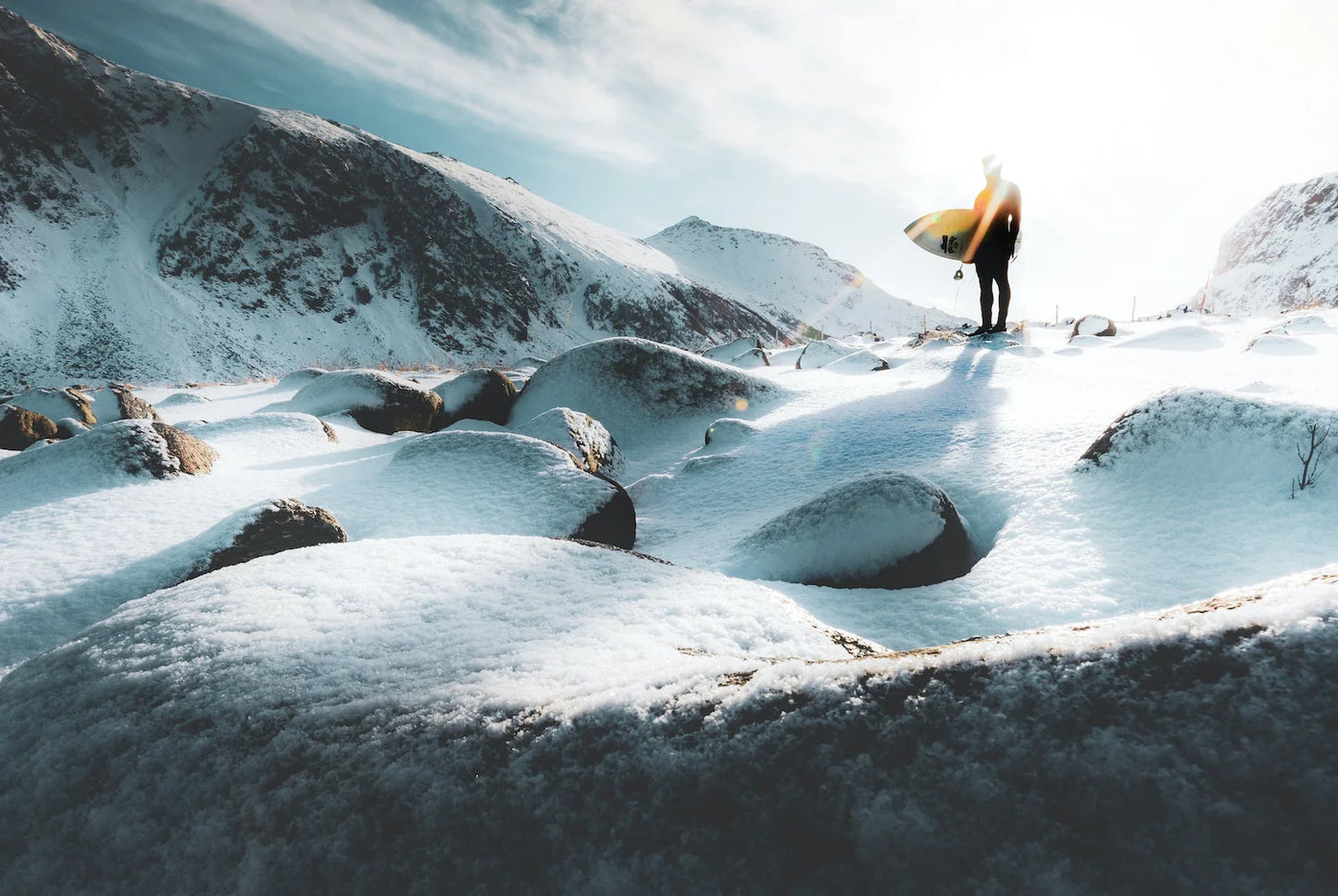 Person with a surfboard standing on a snowy landscape