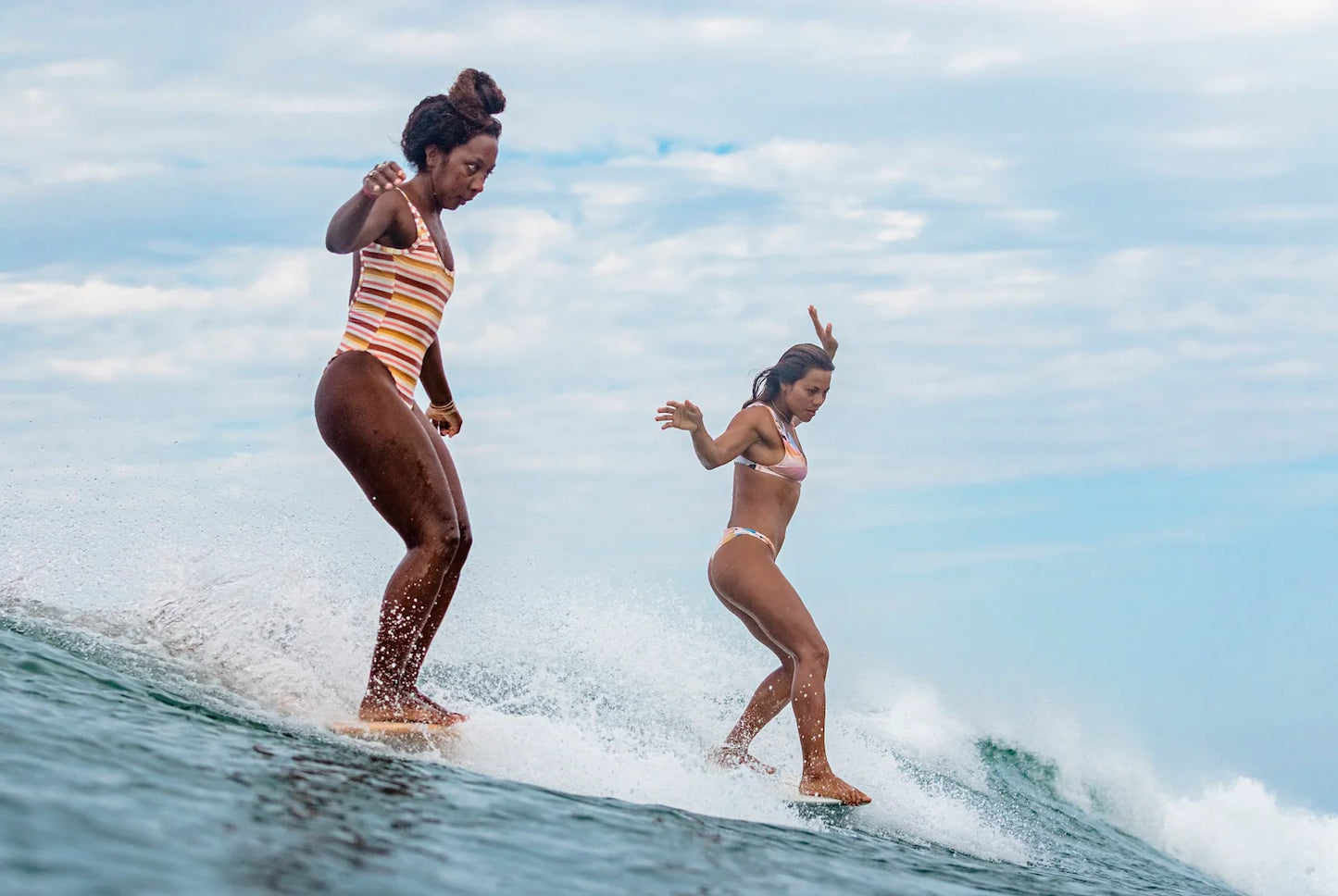 Two women surfing on a wave with a clear sky in the background