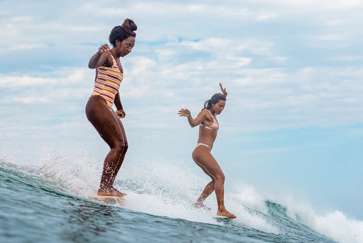 Two women surfing on a wave with a clear sky in the background