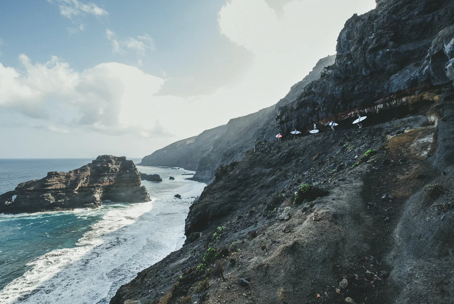 Scenic view of a rocky coastline with people on a cliff edge.