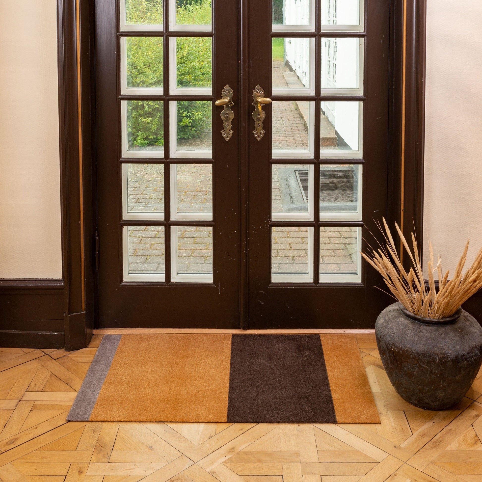 Brown wooden door with glass panels in a room with a parquet floor and decorative vase.