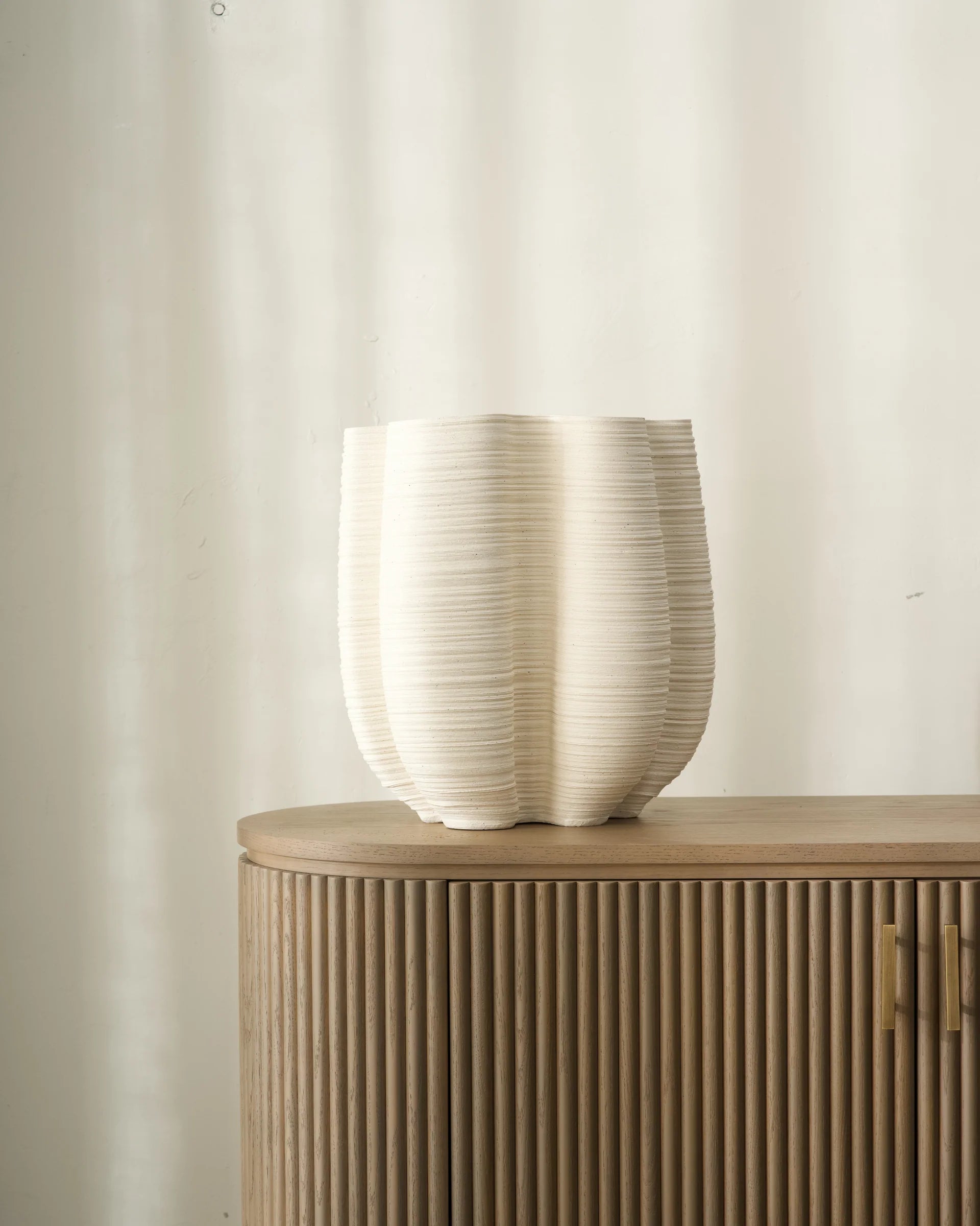 Beige ceramic vase on a wooden sideboard against a plain wall