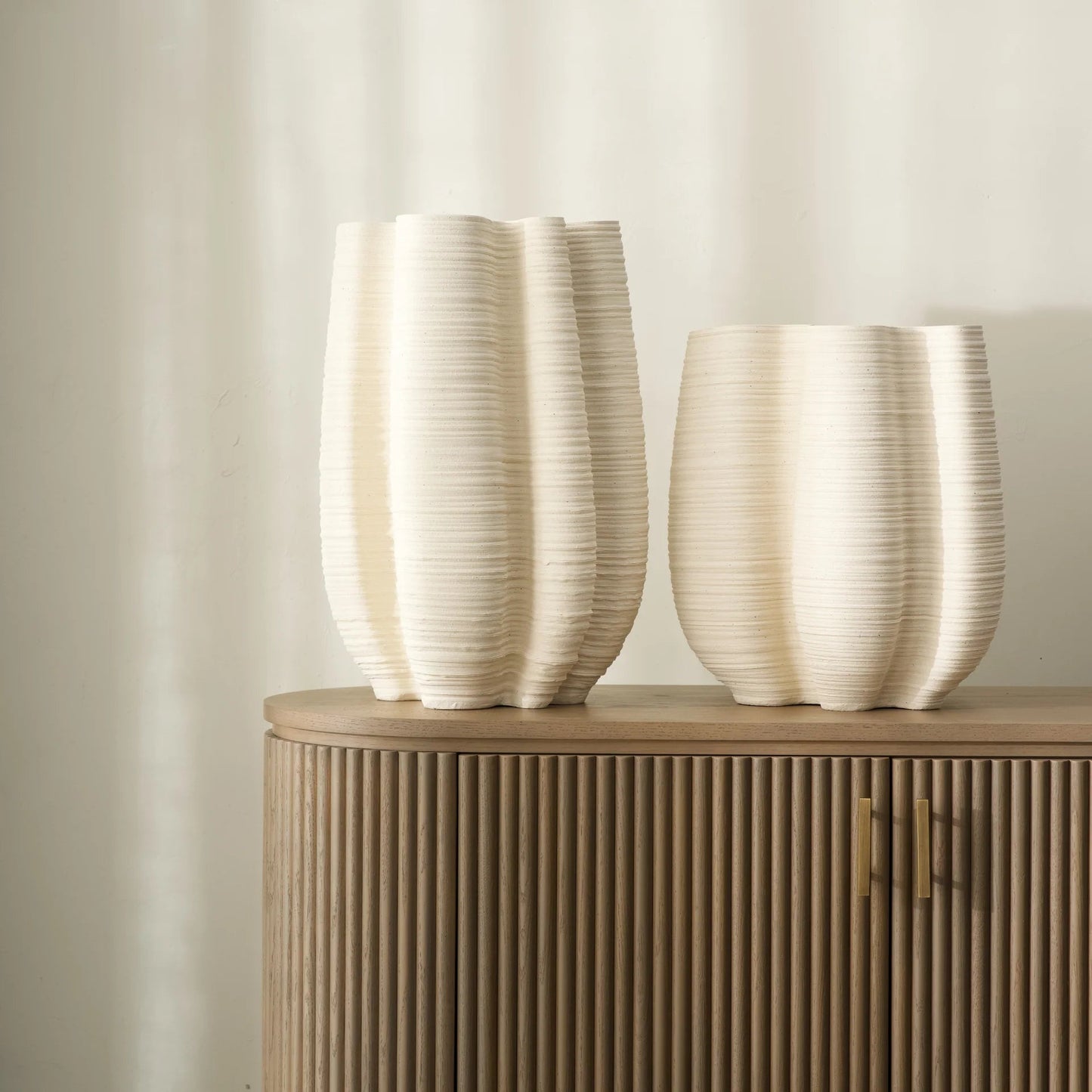Two white textured vases on a wooden cabinet against a beige wall