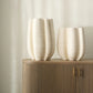 Two white textured vases on a wooden cabinet against a beige wall