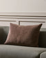 Quilted brown pillow on a gray sofa against a beige wall.