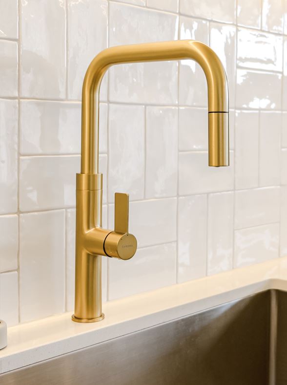 Gold kitchen faucet mounted on a tiled wall with a sink below.