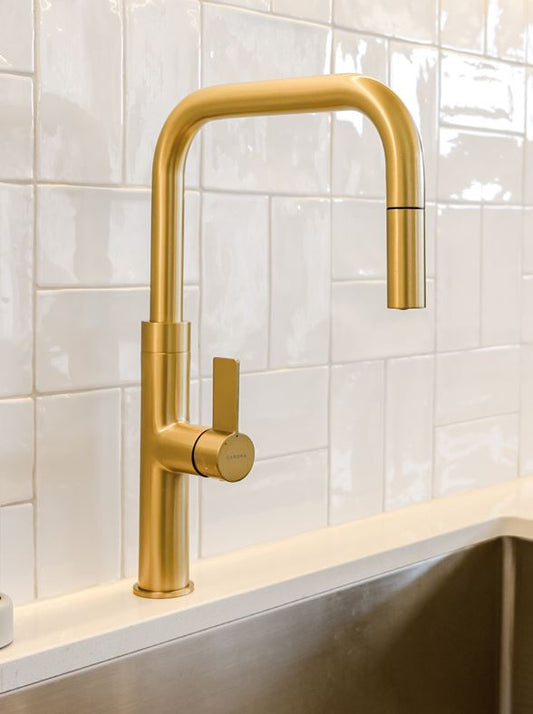 Gold kitchen faucet mounted on a tiled wall with a sink below.