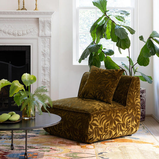 Living room with a patterned armchair, fireplace, and large window with plants.