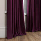 Pair of purple curtains hanging in a window with a wooden floor and neutral wall.