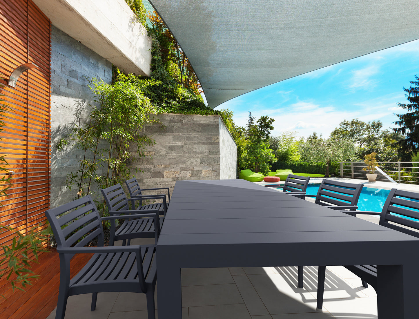 Outdoor dining area with a large black table and chairs near a pool.