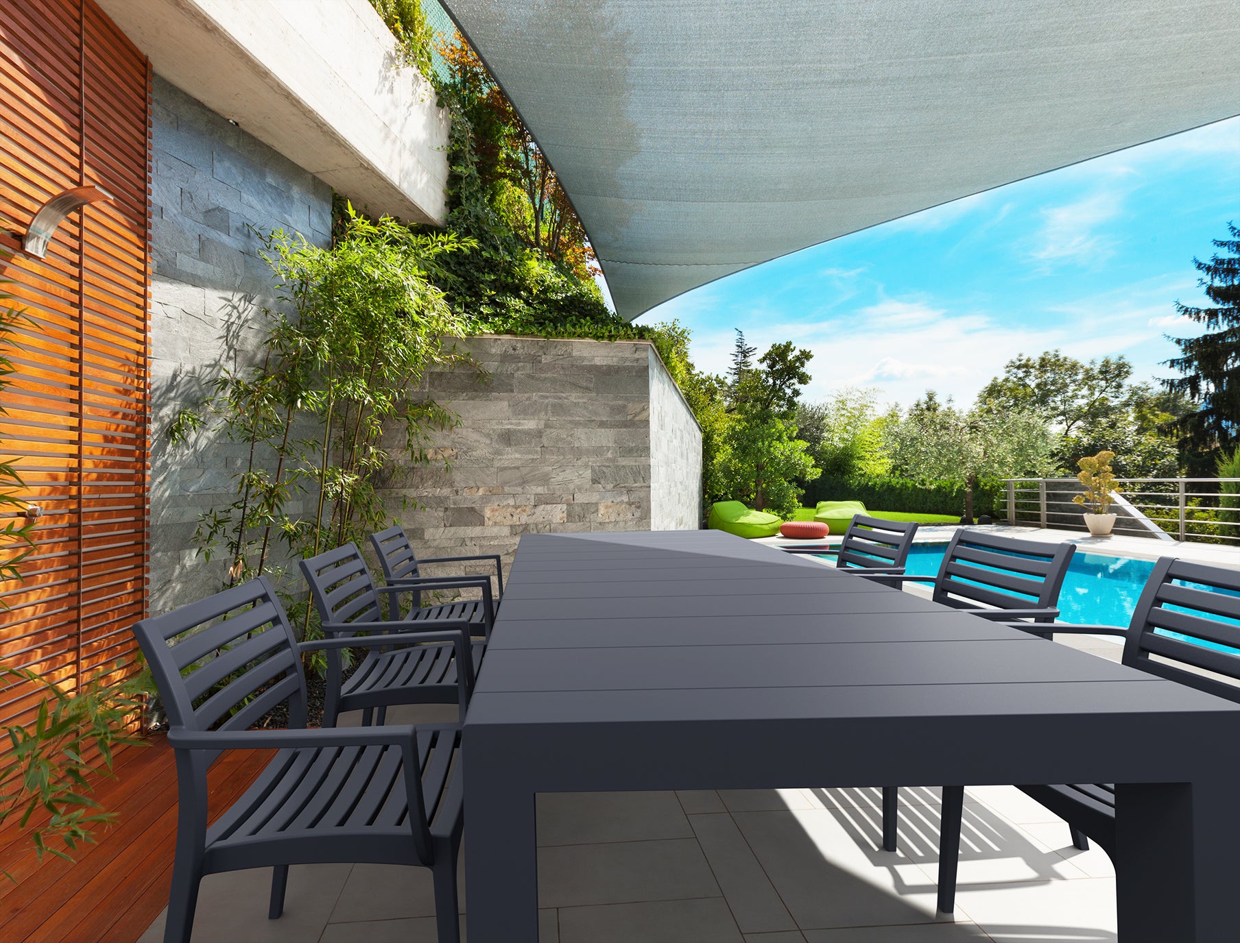 Outdoor dining area with a large black table and chairs near a pool.