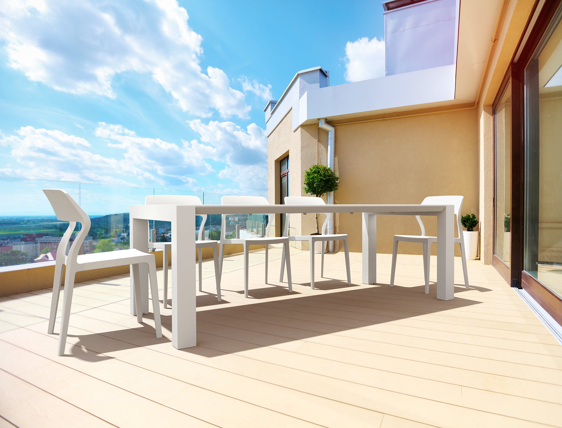 White outdoor dining table and chairs on a wooden deck with a clear blue sky.