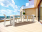 White outdoor dining table and chairs on a wooden deck with a clear blue sky.