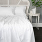 White bed with a wicker headboard and a side table with decor items in a bedroom setting.