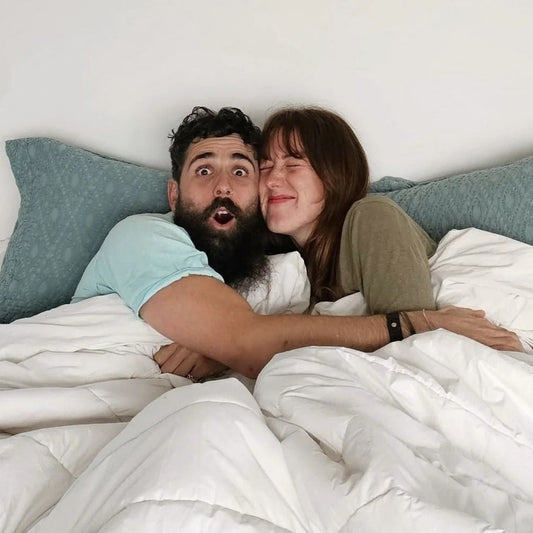 Two people lying in bed together, embracing under a white comforter.