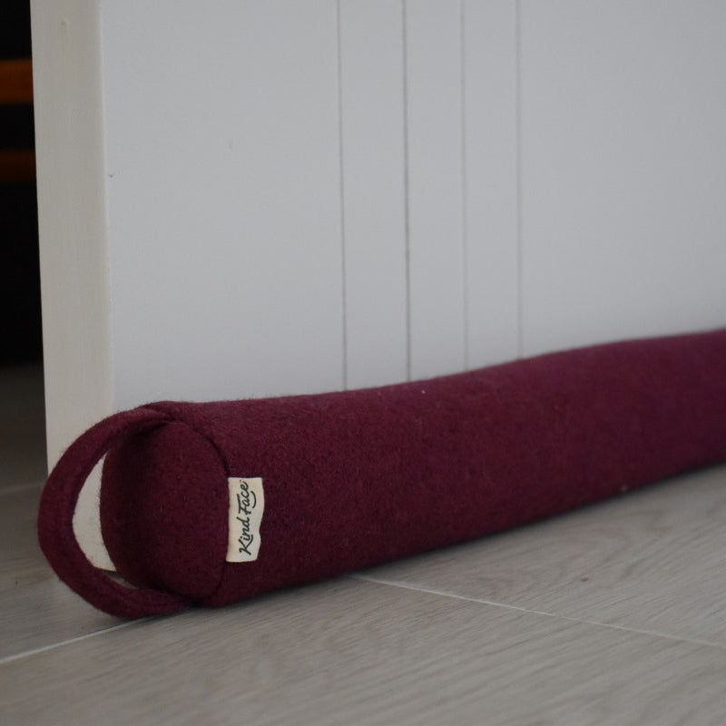 Maroon yoga mat rolled up with a brand tag on a light wooden floor.