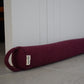 Maroon yoga mat rolled up with a brand tag on a light wooden floor.