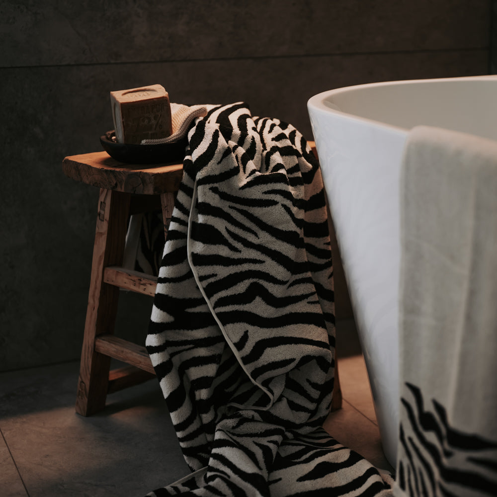 Zebra-patterned towel draped over a wooden stool next to a white bathtub.