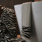 Zebra-patterned towel draped over a chair next to plain towels on a wooden surface.