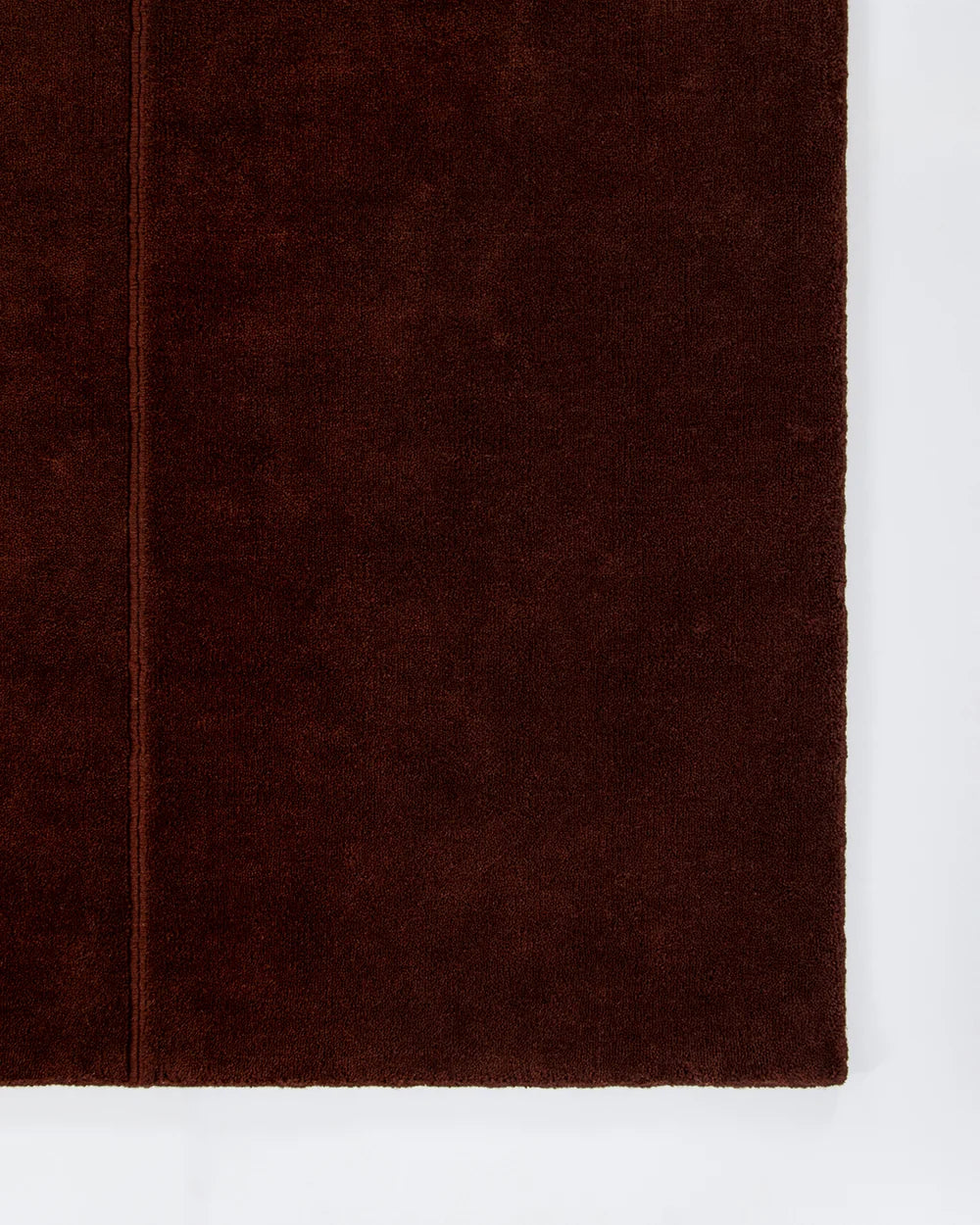 A close-up of a dark red textured wool rug, showing its soft, nubby surface and a stitched edge, set against a plain white background.