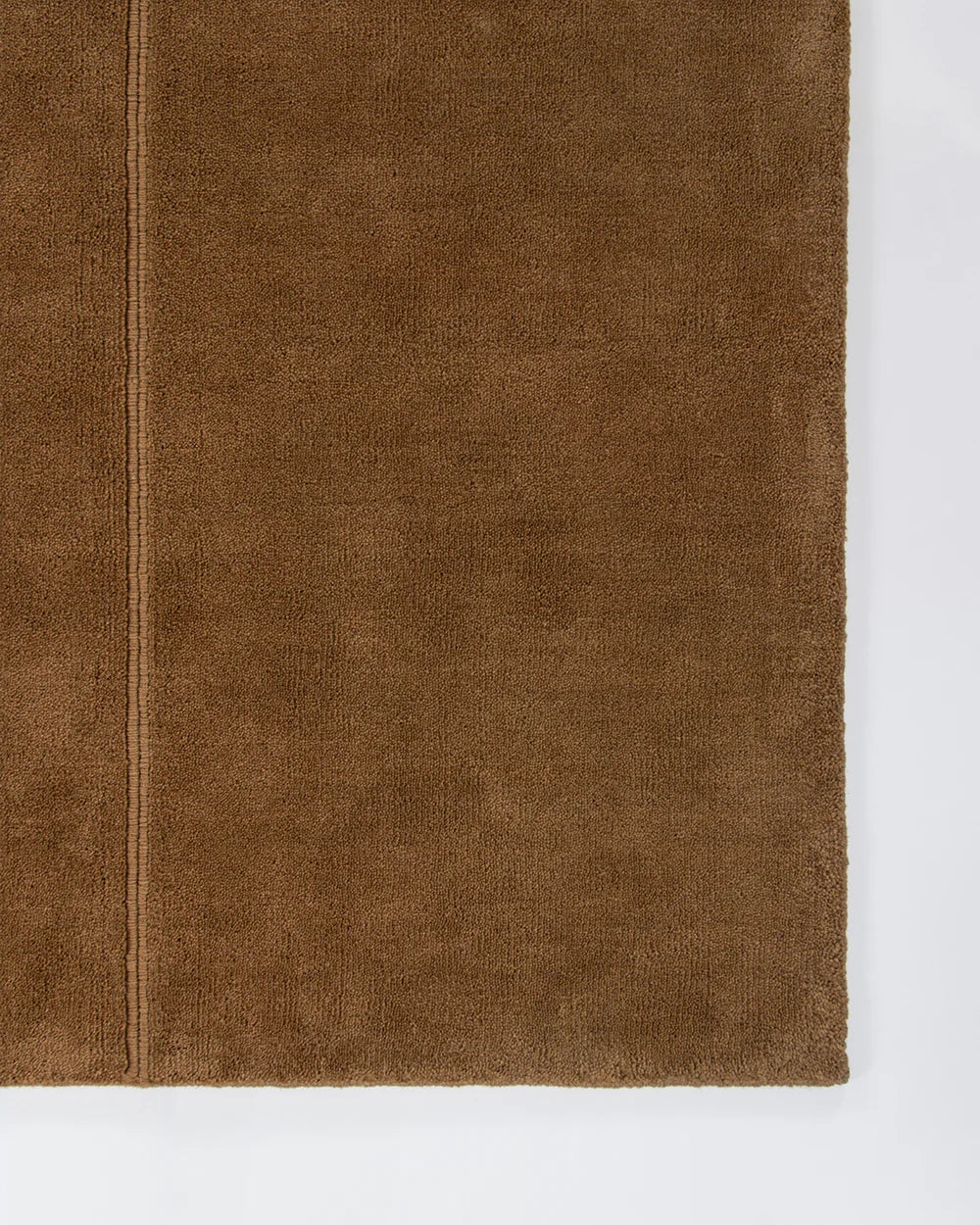 A close-up of a brown wool rug, likely a  showing its soft pile and a stitched seam, set against a plain white background.
