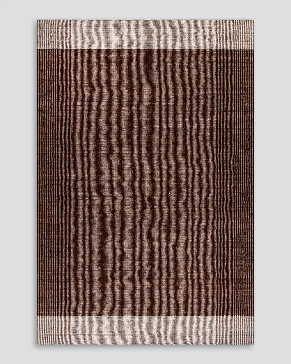 A rectangular woven rug with a textured, cross-hatched pattern in shades of brown and beige, featuring a solid dark brown center and striped borders in beige and brown, shown against a light gray background.